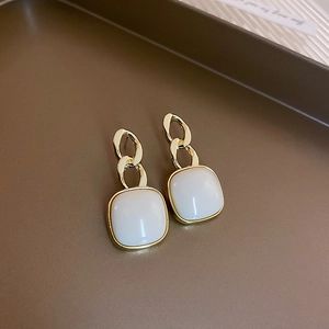 Detailed close-up of 925 silver needle gold earrings with square white opal inlay on tray