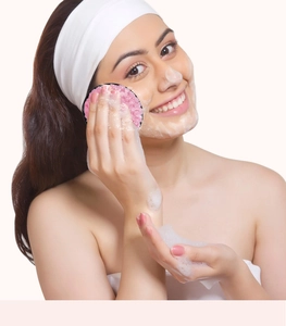 Woman using pink pineapple textured facial cleansing puff with foam on her cheek