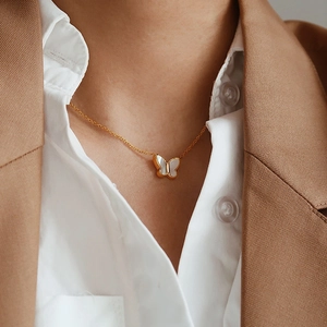 Close-up of elegant gold butterfly necklace with white shell inlay worn by a model