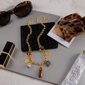 Close-up of vintage gold chain necklace with tiger eye and ceramic pendants on a chic desk
