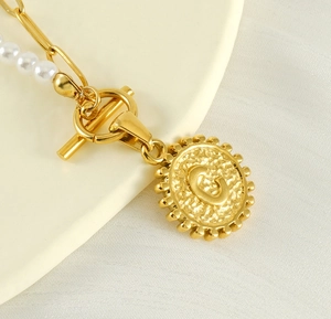Macro shot of gold pearl and paperclip chain necklace with a letter C pendant and OT clasp