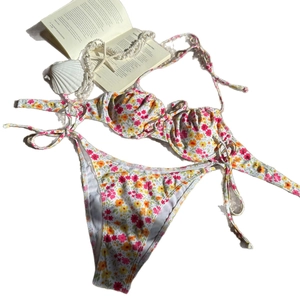 Zweiteiliger Bikini mit Blumendruck, Bügel-Top und seitlich gebundener Hose auf weißem Grund