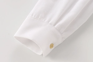 Close-up of white shirt cuff with a gold button and fine linen blend fabric texture