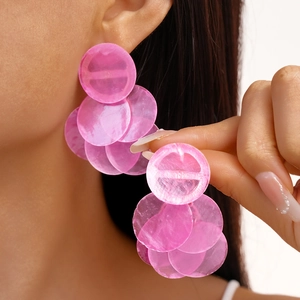 Close-up of pink layered shell-textured round fringe earrings worn by a model