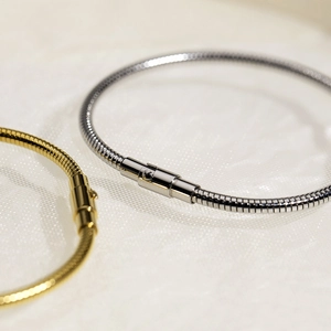 Detail of gold and silver snake bone bracelets with polished clasps on white fabric