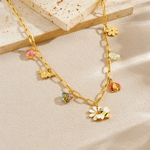 Golden necklace set with floral bee and ladybug charms on a light stone surface