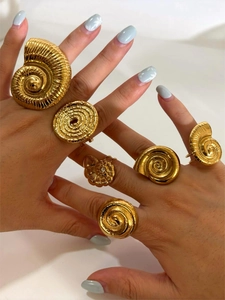 Detailed view of multiple golden shell-shaped spiral rings worn on fingers with metallic finish