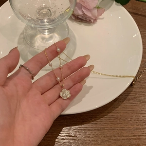 Elegant gold chain necklace with white flower pendant and pearls held by hand