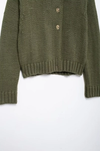 Dettaglio del cardigan in maglia verde militare con polsini a coste e bottoni in metallo