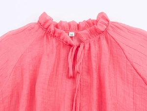Close-up of pink ruffled stand collar with tie-up detail on bohemian pleated fabric