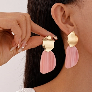Boucles d'oreilles dorées irrégulières avec pendentifs en résine rose sur modèle