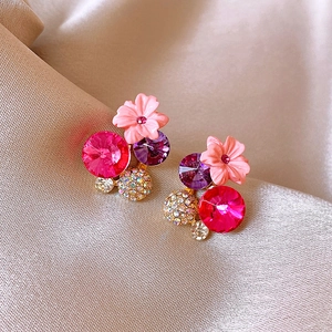 Macro shot of silver needle earrings featuring pink flowers and purple faceted crystals