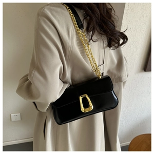 French retro black leather underarm bag with gold geometric buckle on a beige trench coat