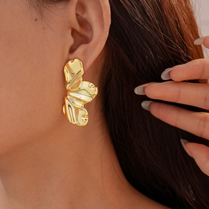 Macro close-up of a model wearing large abstract golden leaf earrings with metallic texture