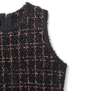 Dettaglio di tessuto in tweed nero con motivo a quadri rosa e giallo su top senza maniche