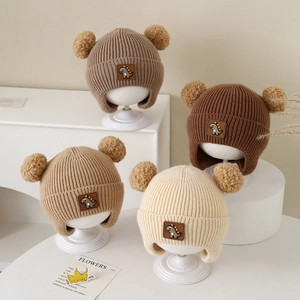 Detailed close-up of knit hats with dinosaur patches and dual pom-poms in earth tones