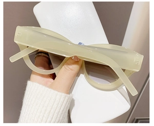 Detail of cream cat-eye sunglasses with dark grey lenses held over a white case