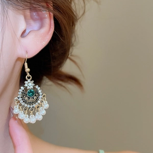 Dettaglio macro di orecchini vintage con gemma verde e perle bianche pendenti