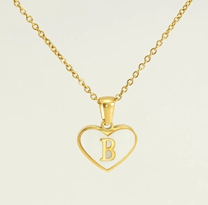 Detail of a golden heart necklace featuring a white shell inlay and the letter B pendant