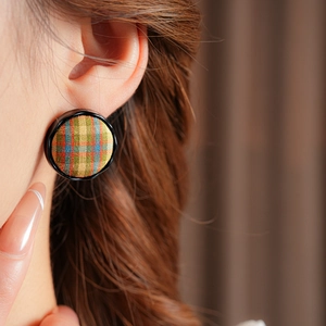 Close-up of a model wearing circular plaid fabric stud earrings in a vintage style