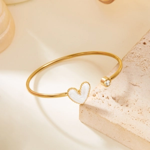 Detailed close-up of a gold heart cuff bracelet with white enamel and a sparkling diamond