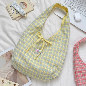 Flat lay of a yellow and blue plaid tote bag with bow detail on a white textured bed