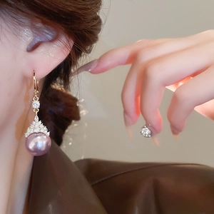 Gros plan de boucles d'oreilles dorées avec perles mauves élégantes et cristaux brillants