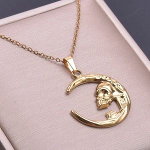 Macro shot of gold moon and skull necklace pendant resting in a beige jewelry box