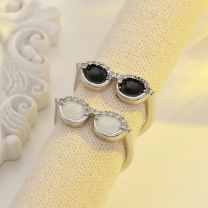 Detail of creative sunglasses-shaped rings with zircon accents on a white knit stand