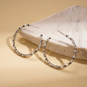 Macro detail of silver geometric twisted C-shape earrings on a white stone background