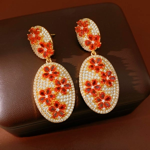 Close-up of vintage oval gold earrings with white zircon pavé and red flower pattern