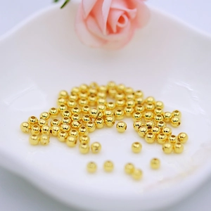 Detailed view of polished 18K gold-plated round spacer beads in a ceramic tray