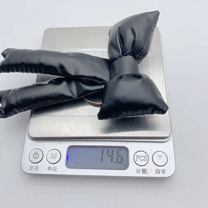 Macro shot of a black metallic puffy bow keychain showing a weight of 14.6g on a digital scale