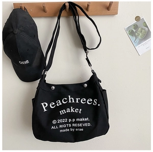 Detailed close-up of a black canvas tote bag featuring white letter printing and silver metal buckle