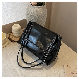 Minimalist black leather underarm bag with gold chain strap shown in a lifestyle setting