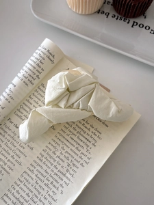 Detailed view of beige pleated fabric hair scrunchie styled on a lifestyle magazine background