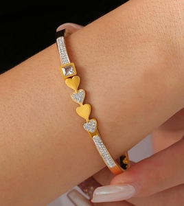 Detailaufnahme eines vergoldeten Herzarmbands mit Zirkonia und quadratischem Diamanten