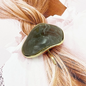 Detail of a golden irregular hair pin with grey marble inlay in a braided hairstyle
