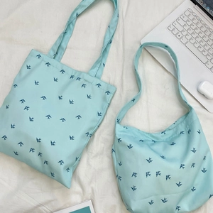 Detail view of light blue canvas tote and crescent bag with navy bird prints on white cloth