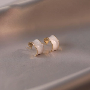 Detailed view of 18K gold plated C-shape earrings with white enamel on champagne silk