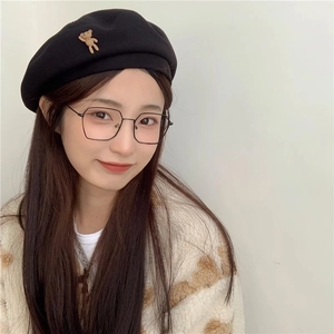 Detail of a black wool beret featuring a 3D brown teddy bear brooch and stylish glasses