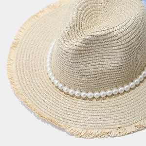 Close-up of straw sun hat featuring elegant faux pearl trim and frayed raw edge detail