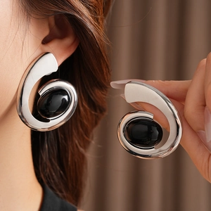 Detail of silver spiral earrings with black oval stones shown on ear and held by hand