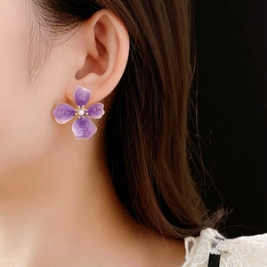 Détail des boucles d'oreilles fleurs mauves émaillées avec perle sur le mannequin