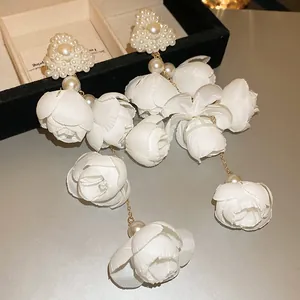 Detailed close-up of large white fabric camellia floral drop earrings with pearl studs