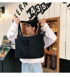 Détail d'un grand sac cabas noir en toile avec deux poches avant et un design spacieux