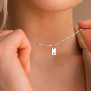 Detailopname van een zilveren vierkante hanger met letter A gedragen door model