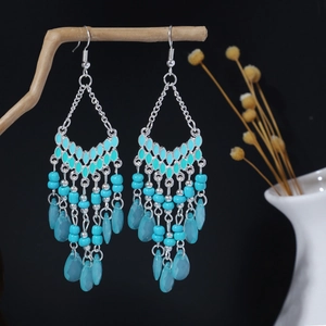 Dettaglio di orecchini boho con perle turchesi e nappe appesi a un ramo di legno