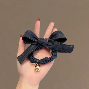 Chouchou en jean bleu marine avec noeud et breloque cloche coeur dorée tenu à la main