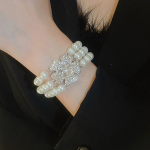 Close-up of three-strand faux pearl bracelet with a sparkling clover diamond pendant